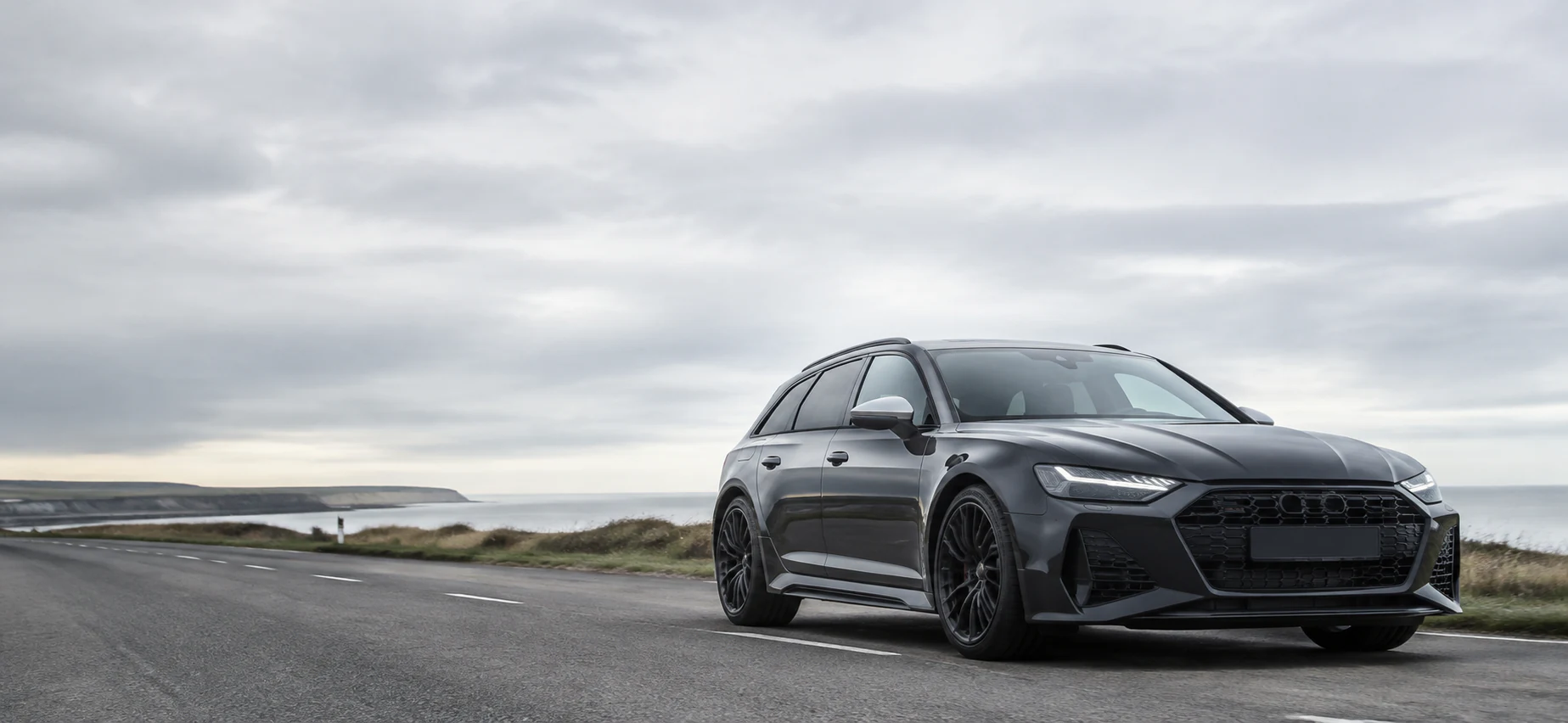 A modern dark estate car on a quiet British coastal road